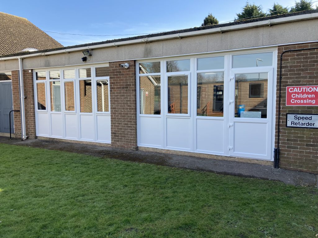 A replacement double set of windows and panels in white at school building with a fire escape door at one end
